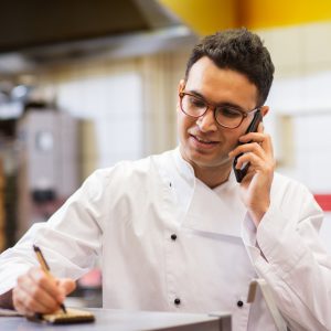 people, fast food and cooking concept - chef at kebab shop writing order and calling on smartphone