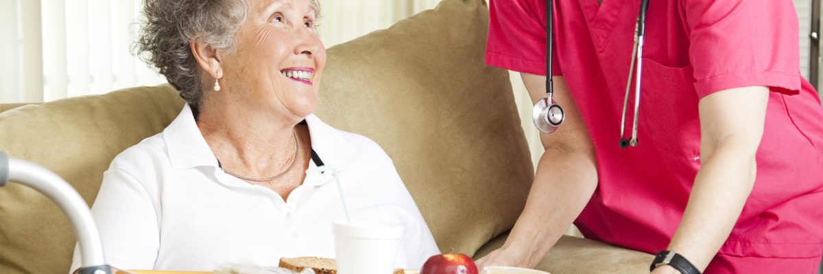 Retired senior woman in nursing home gets lunch from a caring nurse.